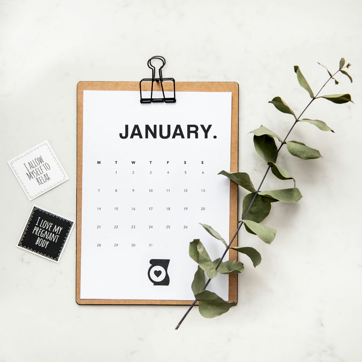 Monthly calendar on a clipboard next to a green plant
